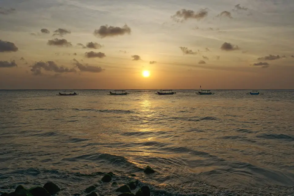 Bali sahilində qızılı günbatımı və üfüqdə ənənəvi balıqçı qayıqları