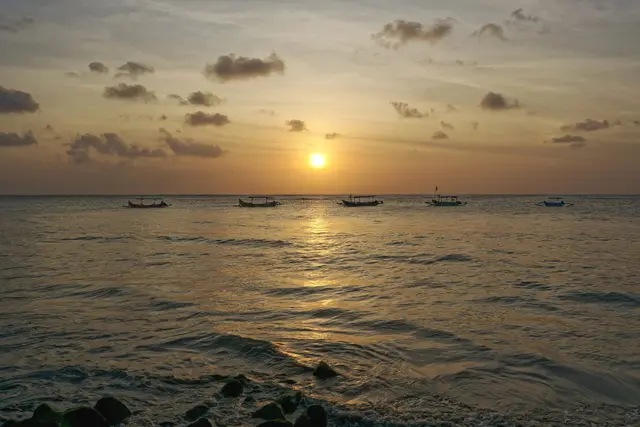 Bali sahilində qızılı günbatımı və üfüqdə ənənəvi balıqçı qayıqları
